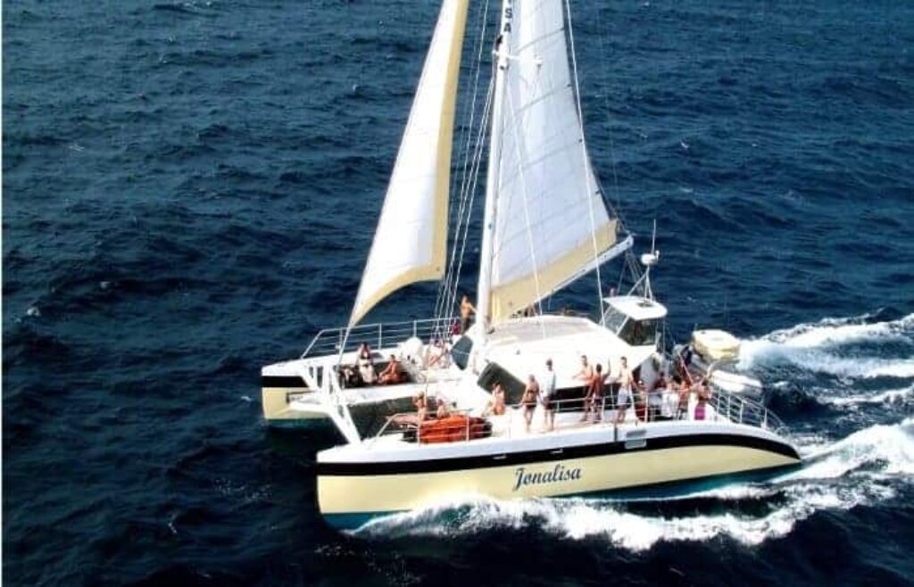 During the Klein Curacao Adventure, a white-and-yellow catamaran sails across deep blue waters as guests relax on deck and enjoy sunny skies—the perfect way to experience a true Curacao adventure.