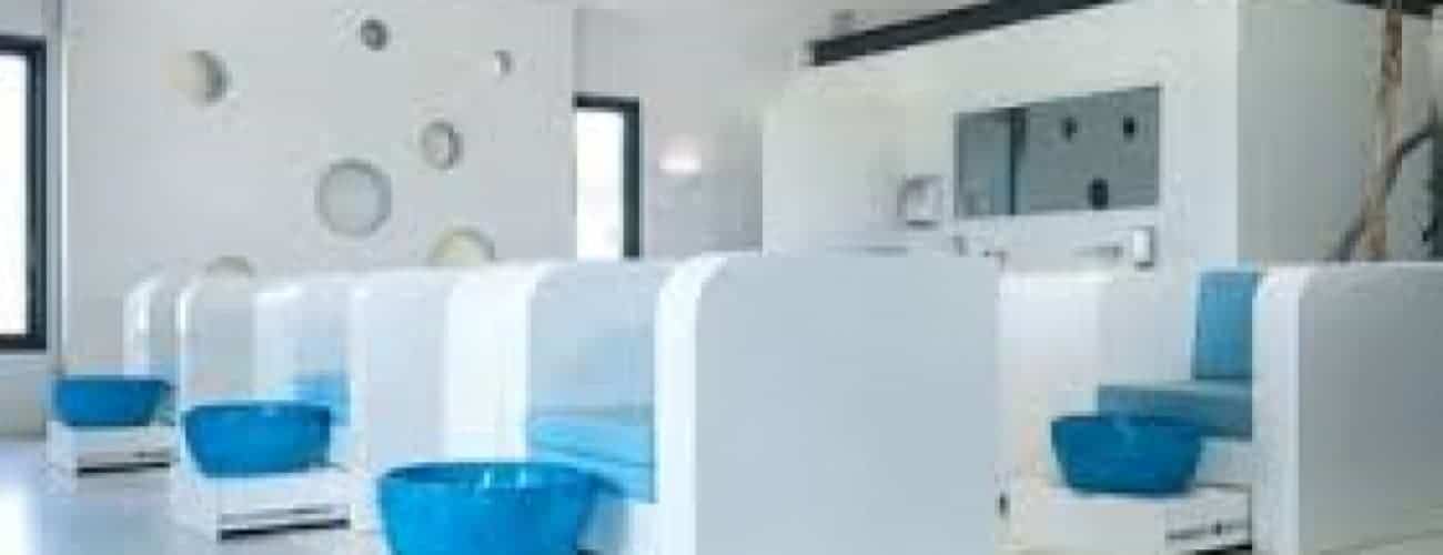 Het interieur van een moderne nagelstudio bestaat uit witte pedicurecabines met blauwe kussens en bijpassende schalen. Grote ramen en ronde muurdecoraties creëren de perfecte omgeving voor Een moment van ontspanning.
