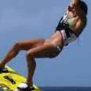 Una persona realiza una demostración de arranque en el agua sobre una tabla amarilla, en el aire sobre el agua, como se muestra en "Lección para principiantes 4 - Arranque y conducción en el agua", con el cielo azul y el horizonte de fondo.