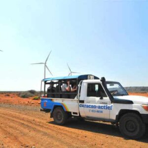 Three images: Ocean water shoots up through blowholes; tourists enjoy the Breath of Curacao Jeep Tour, driving by wind turbines; a rocky coastline is hit by waves under a partly cloudy sky.