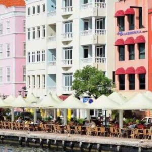 Experience the East and City Tour: stroll along a waterfront promenade lined with Dutch-style buildings, vibrant facades, and outdoor cafes shaded by yellow umbrellas—perfect for enjoying the lively city atmosphere.