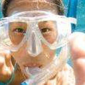 With "Everyone can snorkel!" swim goggles, a snorkeler faces the camera underwater with hands reaching forward; their facial features are visible through the clear goggles amid shimmering blue water and bubbles.
