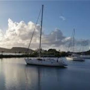 Three white sailboats from the "Half day sail tour" float on calm water, their reflections visible. The partly cloudy sky and sun’s soft light create a tranquil harbor scene with lush green hills and rocky islands in the background.