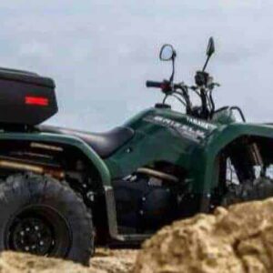 A Half day Westside ATV Adventure vehicle with large tires and a rear storage box sits on rocky shore facing the ocean, framed by tan rocks and a cloudy sky in this rugged coastal setting.