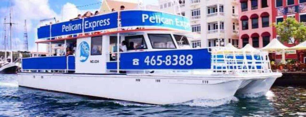 The white and blue Pelican Express catamaran offers the Harbour Trip, sailing near colorful waterfront buildings. Passengers ride on the upper deck under a clear sky. For details, call 465-8388.