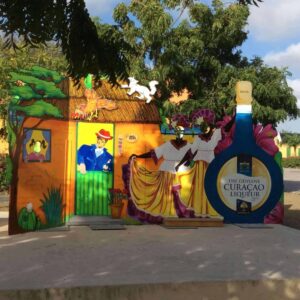 A vibrant cutout display for the Island and Beach Tour features two women in yellow skirts dancing, a man in blue by a green door, tropical plants, and colorful buildings—capturing the lively spirit of an island adventure.