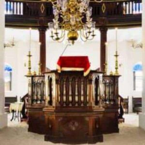 The Jewish Heritage Tour features the interior of a historic synagogue with white walls, tall columns, dark wooden pews, a red-draped bimah, gold chandeliers, and sunlight streaming through arched windows—a true tour highlight.