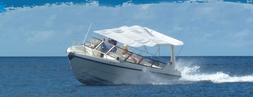 The Klein Curacao Speedboat Adventure taxi service speeds across calm blue water with several passengers seated under a white canopy, enjoying the ride and ocean spray beneath a partly cloudy sky.