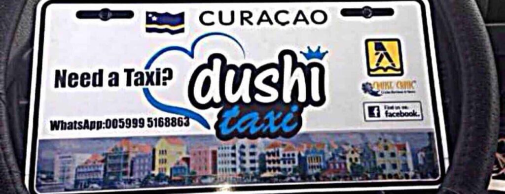 The "Taxi to L'aldea" sign from Curaçao says, "Need a Taxi? dushi taxi," with a heart graphic. Contact via WhatsApp at +0059995168863. Features the Curaçao flag, Quick Chip logo, Facebook icon, and Willemstad's colorful waterfront.