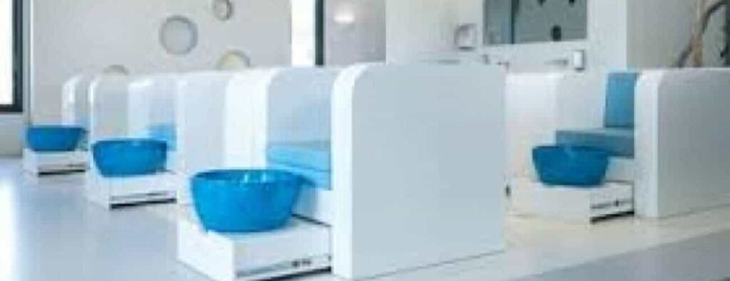 A bright, modern nail salon with white pedicure stations featuring cushioned blue seats and glossy blue foot basins. Circular wall décor and large windows create a clean vibe—ideal for your next Laman Manicure.