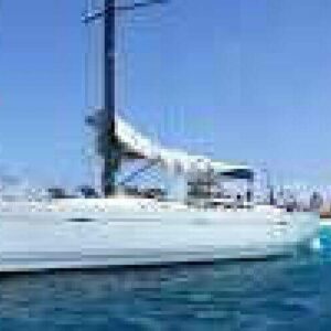 The Local Day trip watersport features a white sailboat with sails down, floating on clear blue water near a sandy coast under a bright sky. Perfect for local outings, guests enjoy sunny weather and watersport activities on deck.