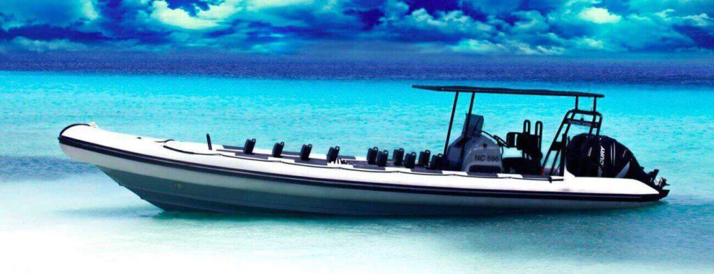 De Powerboat - speedboot - boottocht: 30 minuten pleziertocht is een gestroomlijnd wit opblaasbootje met zwarte bekleding, zwarte stoelen, een overkapping en twee buitenboordmotoren, voor anker in helder turquoise water onder een felblauwe hemel.