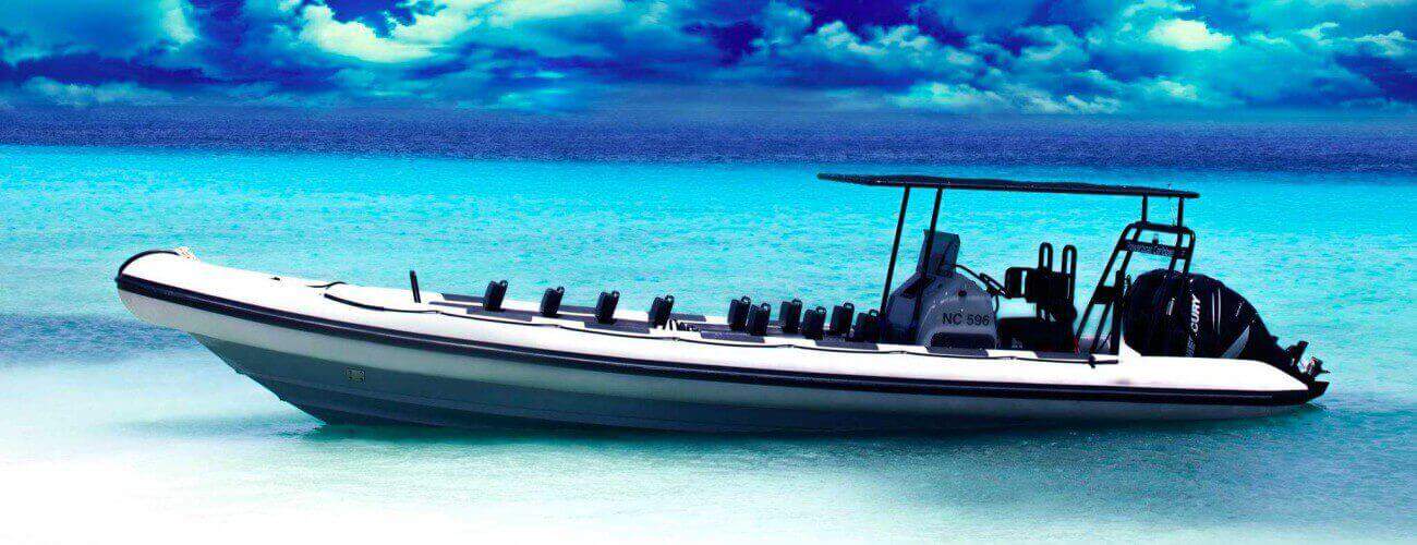 De Powerboat - speedboot - boottour 120 minuten hoge snelheidstour, een wit met zwarte opblaasbare boot met meerdere zitplaatsen, een luifel en buitenboordmotoren, ligt voor anker in helder turquoise water onder een dramatisch blauwe hemel.