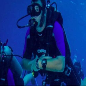 Two scuba divers in purple wetsuits explore the clear blue ocean, possibly practicing skills from the PADI Rescue Diving Course, surrounded by deep water and shimmering bubbles.