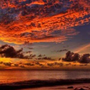 The Romantic Sunset Sail captures a vivid sunset over calm ocean waters with dramatic orange-red clouds, rocky cliffs and trees silhouetted at the edge, and a sailboat drifting by the glowing sun reflected on water and sand.