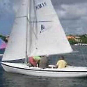 The Sailing course open keelboat, a small white boat for two, glides on calm water with colorful boats and yachts nearby and waterfront houses under partly cloudy skies, creating an ideal setting for relaxed sailing.