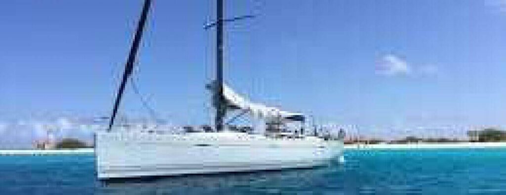 Experience our Sailing Trips Per Day with Overnight Stay: relax on a white sailboat anchored near a sandy beach with turquoise waters and sparse greenery—perfect for day adventures or nights under clear blue skies.