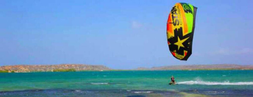 A person takes a Semi private lesson - Kitesurfing on turquoise water under a clear sky, flying a star-decorated kite as rocky hills rise across the bay.