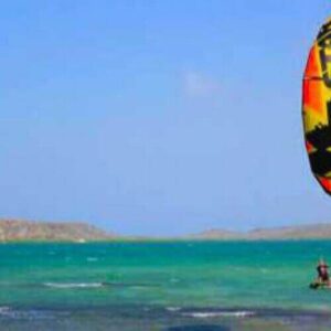 A person takes a Semi private lesson - Kitesurfing on turquoise water under a clear sky, flying a star-decorated kite as rocky hills rise across the bay.