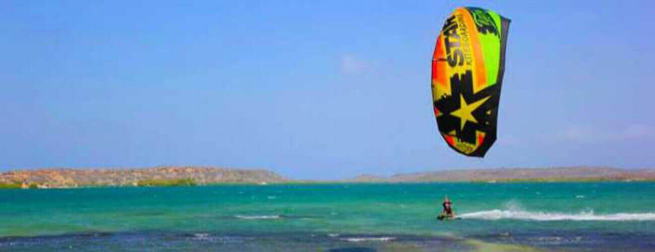 A person takes a Semi private lesson - Kitesurfing on turquoise water under a clear sky, flying a star-decorated kite as rocky hills rise across the bay.