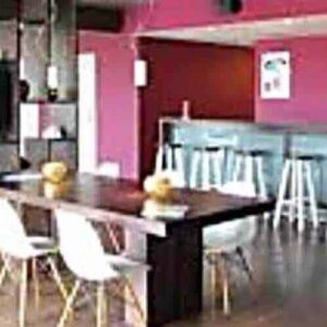 Modern interior with a wooden table, four white chairs, and a bar with high stools. Watch games on the wall-mounted TV and enjoy your Short Term sport Membership. Features dark wood flooring, red accent walls, and decorative shelves.