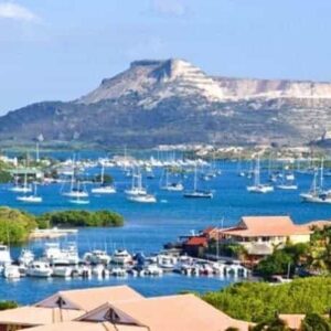 Enjoy the Spanish water Tour: cruise a scenic blue bay dotted with sailboats and yachts, framed by lush greenery, red-roofed buildings, and a flat-topped mountain beneath a clear sky.