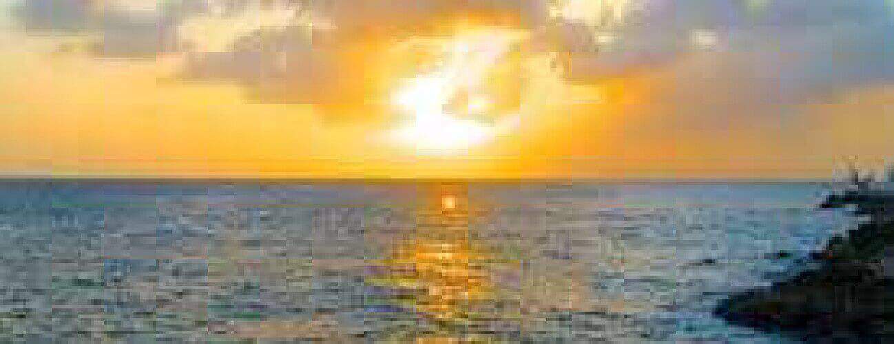 Sunset Spanish Water captures a vibrant sunset with golden light reflecting on the ocean, partly cloudy skies, and rocky silhouettes along the shore, creating a calm and serene atmosphere.