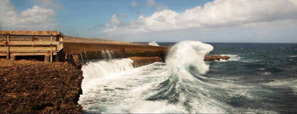 Experience the thrill of waves crashing against a rocky shore under partly cloudy skies as white foam soars above the rocks—all from a wooden viewing platform on the Wonderful World of Water Jeep Tour.