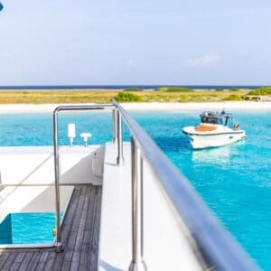 Geniet van het idyllische uitzicht op turquoise water, een zandstrand en weelderig groen vanaf het dek van je jacht met Klein Curacao All-In Reis - een complete reiservaring bij Klein Curacao onder een strakblauwe hemel.