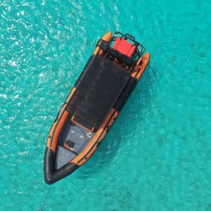 Aerial view of a Powerboat Private Charter with orange and black inflatable sides, covered seating, and a red container at the back floating on clear turquoise water with sunlight shimmering over the sea floor.